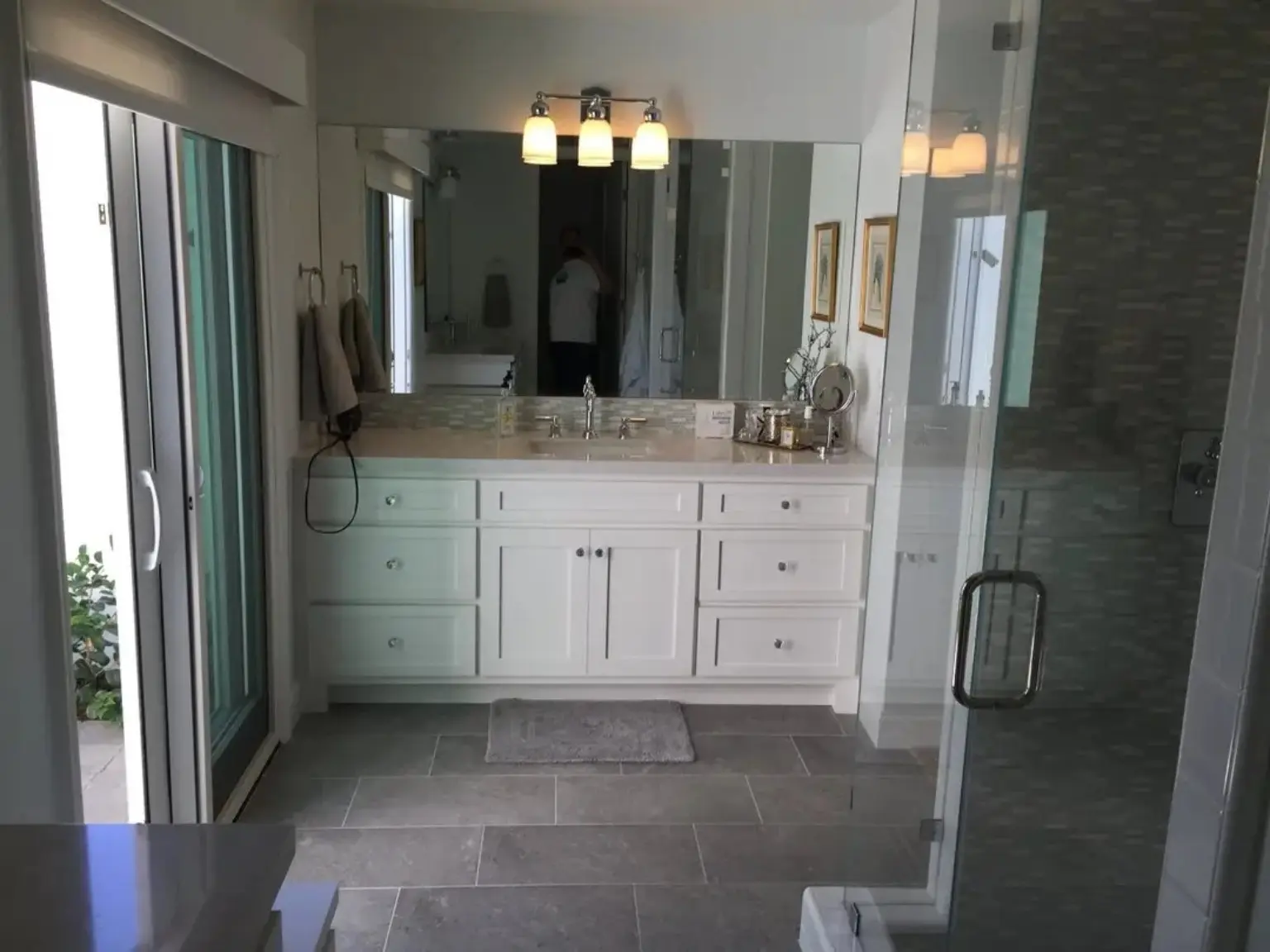 Completed JBI bathroom renovation with white vanity, glass shower, and gray tile