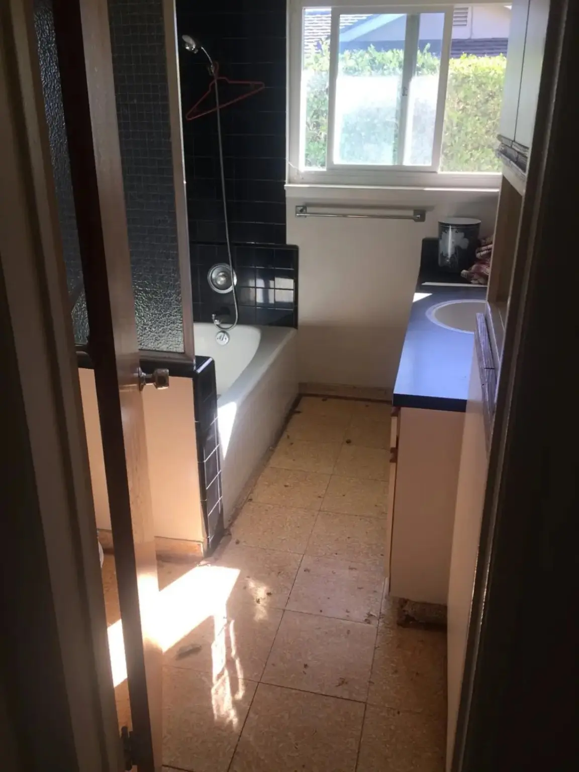 Bathroom before renovation with dark tile tub surround and older vanity