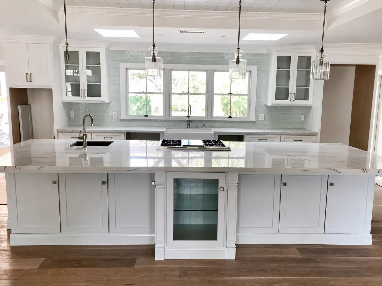 Completed white custom kitchen with a large stone island and pendant lighting