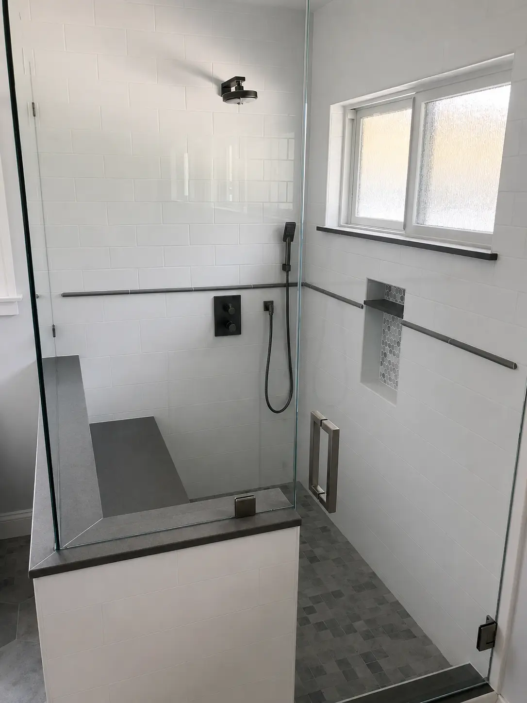 Completed glass-enclosed shower with dark fixtures, bench, and tiled niche