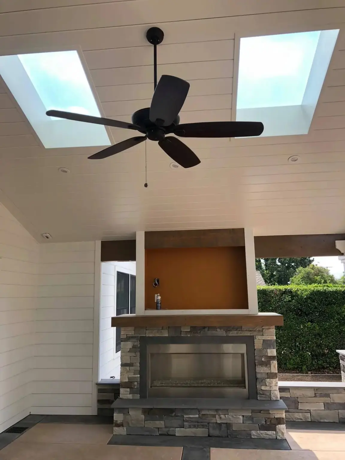 Completed outdoor stone fireplace beneath a skylit covered patio